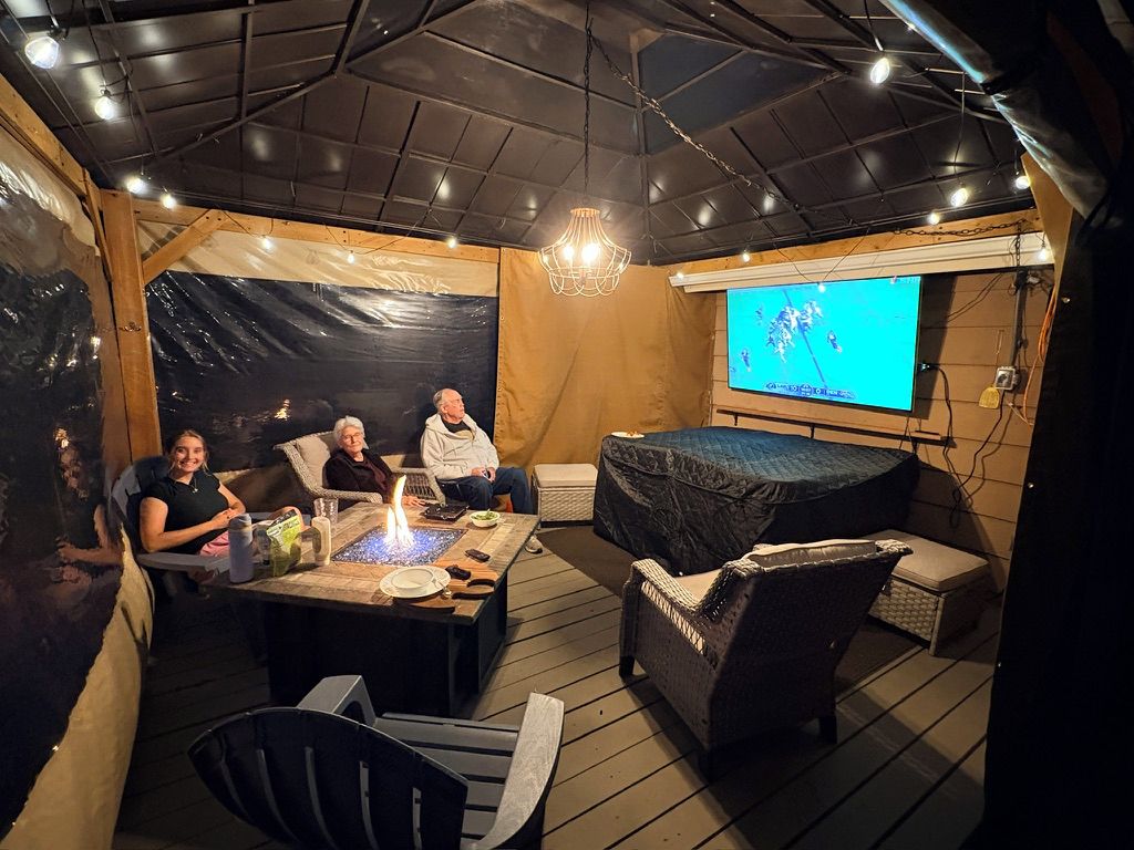 Un espacio exterior acogedor con una chimenea, una pantalla de televisión y una estructura parecida a una carpa.