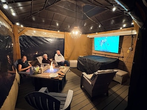 Un espacio exterior acogedor con una chimenea, una pantalla de televisión y una estructura parecida a una carpa.