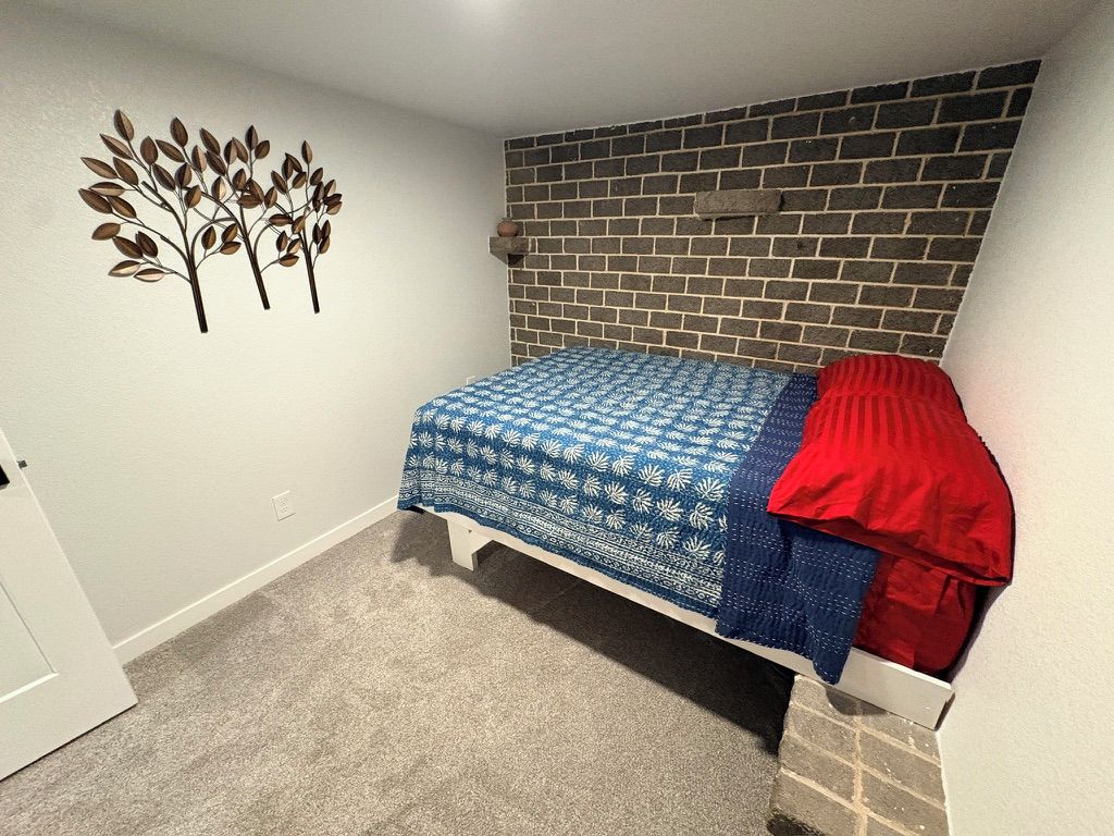 A bedroom with a bed, a brick wall, and a wall decoration.