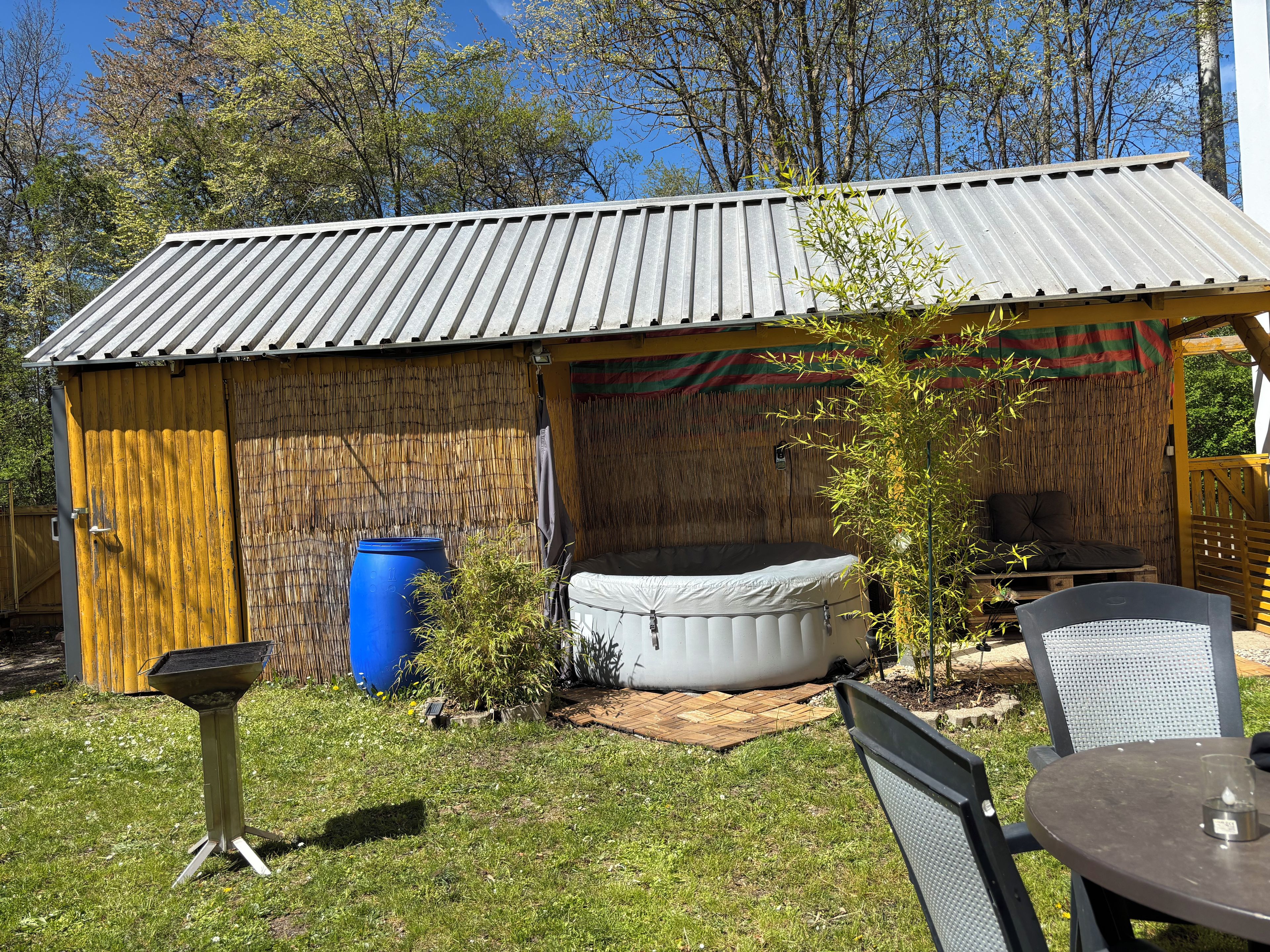 Ein Garten mit überdachter Terrasse, Grill, Whirlpool und Gartenmöbeln.