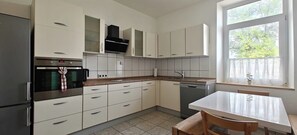 A modern kitchen with white cabinets, a built-in oven, a dishwasher, and a window with a view of trees.