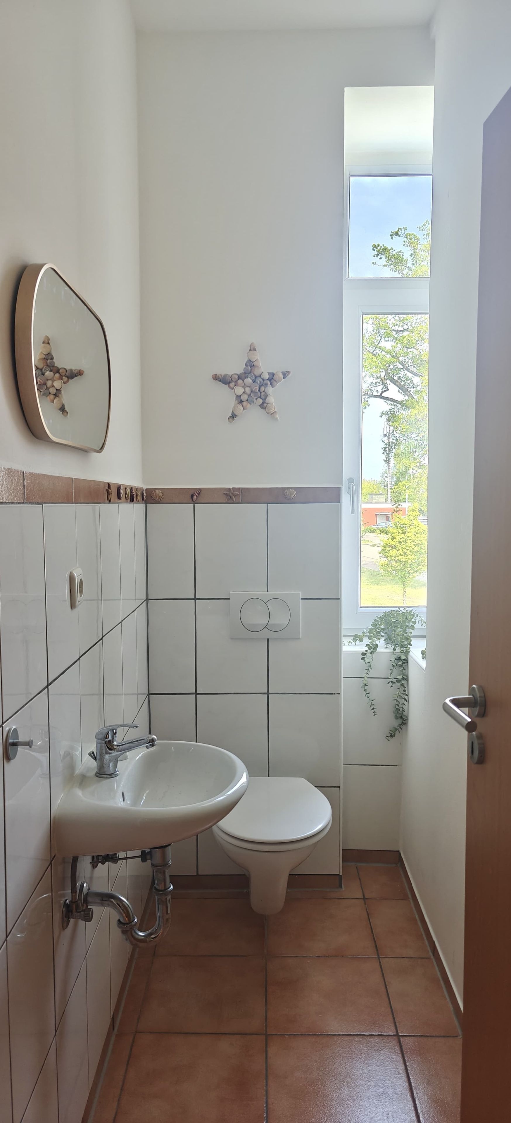 A bathroom with a sink, toilet, and a window with a view of greenery.