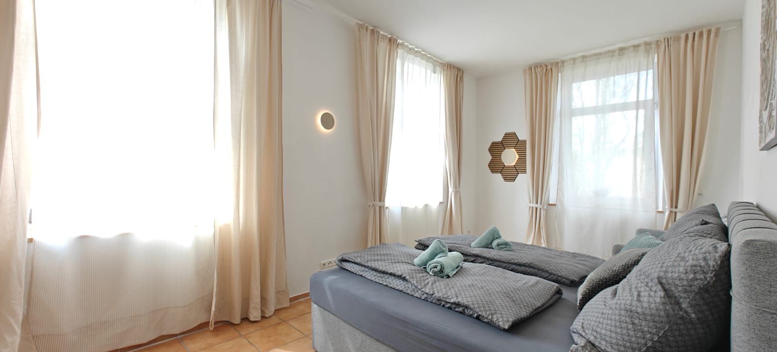 A hotel room with two beds, beige curtains, a wall-mounted light fixture, and a hexagonal mirror.