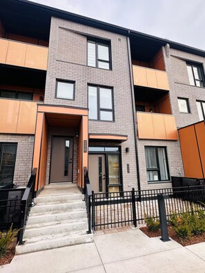 A multi-story apartment building with a modern design, featuring a central entrance with a door and steps leading up to it. - Modern & Cozy Townhouse - 2 Bed + 3 Bath w/Parking (Brampton)
