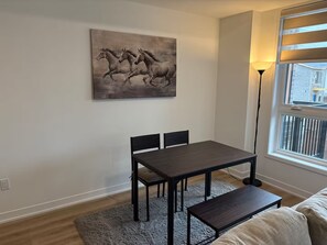 Ein Essbereich mit Tisch und Stühlen, einem Gemälde von Pferden an der Wand, einer Lampe und einem Fenster mit Jalousien.