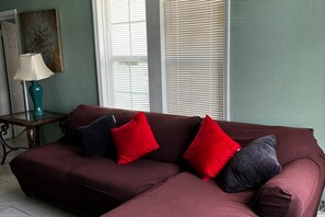 Un sofà modular amb coixinets vermells i foscos, una làmpada color aquamarina sobre una taula auxiliar, i una peça decorativa a la paret.