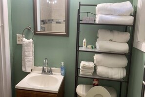Un bagno con lavandino, specchio, asciugamano e uno scaffale con asciugamani.
