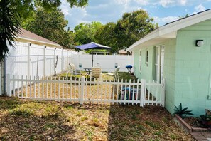 A fenced backyard with a table and chairs, a covered patio area, and a light green building. - Downtown Sarasota House 3br,2ba, Pet-friendly,6ppl (Sarasota)