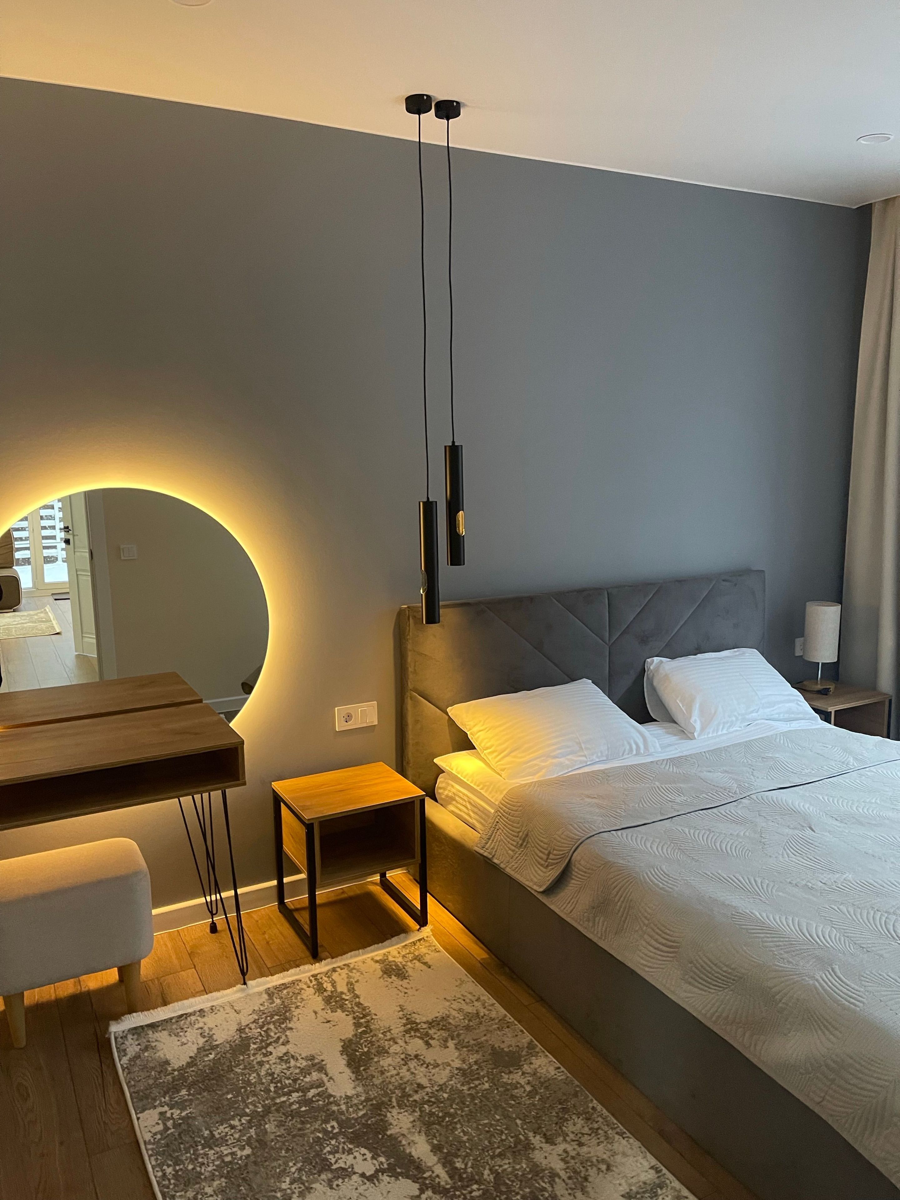Ein modernes Schlafzimmer mit Bett, Nachttisch und einem Spiegel mit runder Beleuchtung.