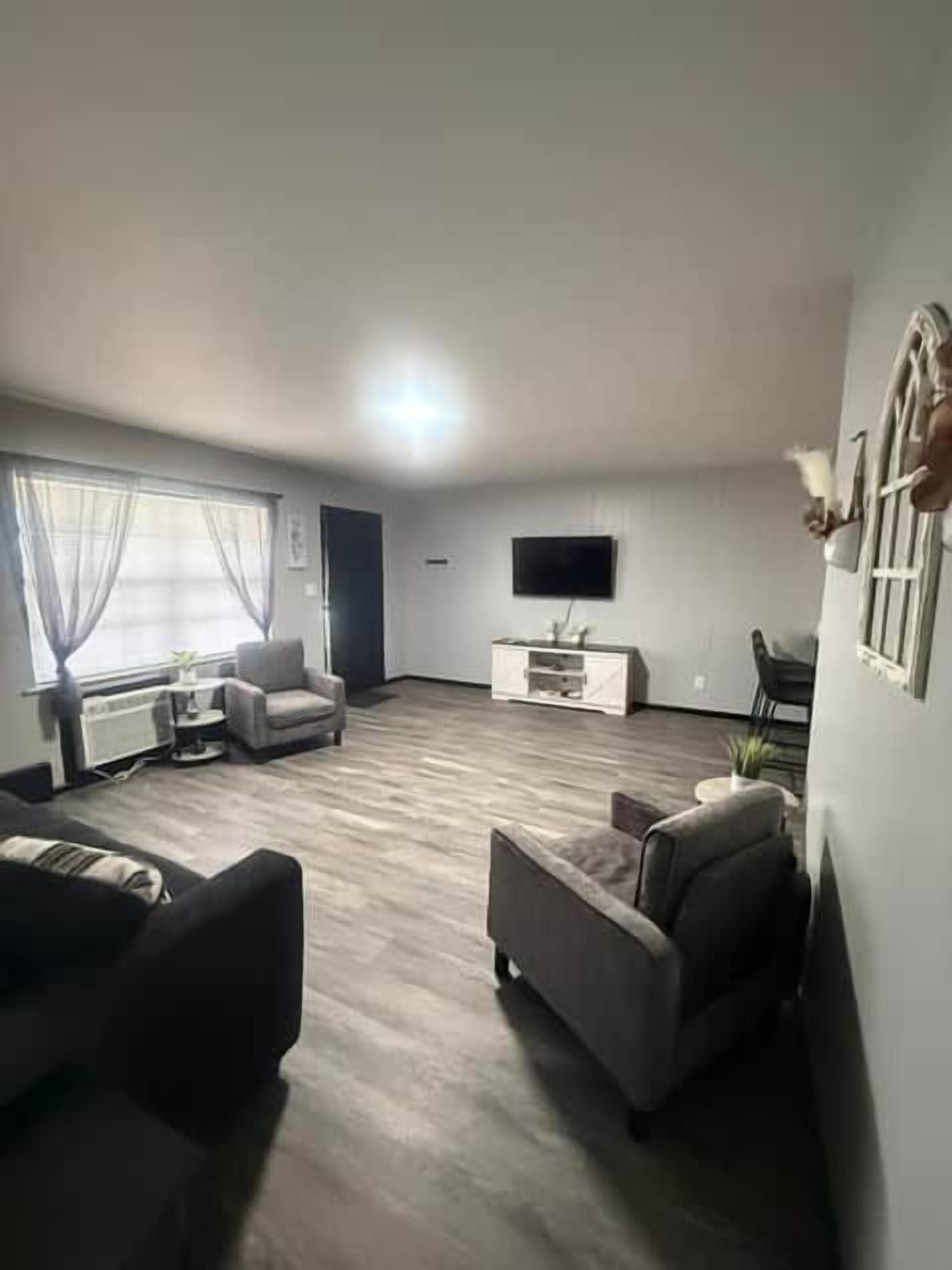 Una sala de estar con televisor de pantalla plana, sofá, mesa de centro y ventana con cortinas.
