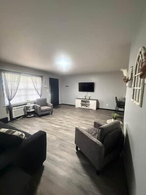 A living room with a flat-screen TV, a sofa, a coffee table, and a window with curtains.