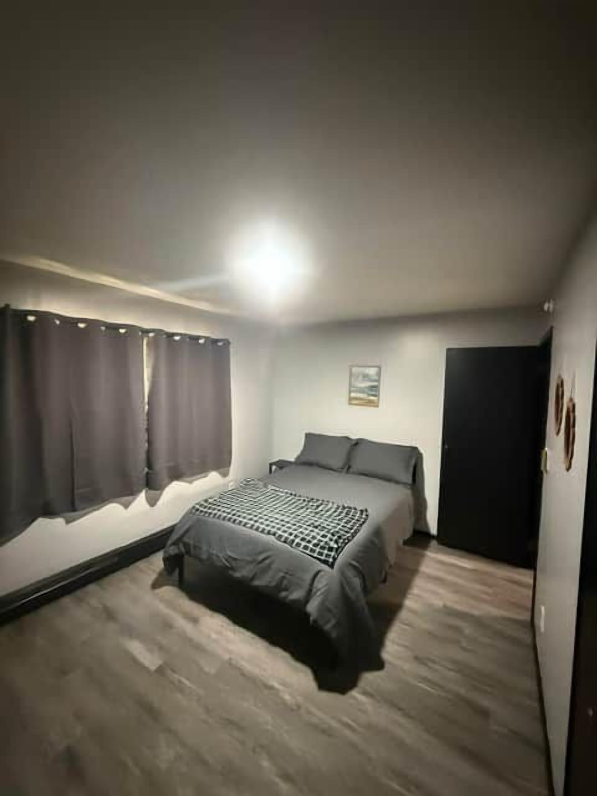 Et soveværelse med en seng, gardiner, en lampe på væggen og en dør.