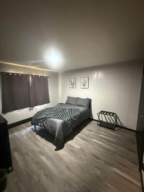 A bedroom with a bed, a window with curtains, a wall-mounted light, and a bed rail. - Welcome Retreat!  A little piece of home. Comfortable Beds!! (Hoopeston)