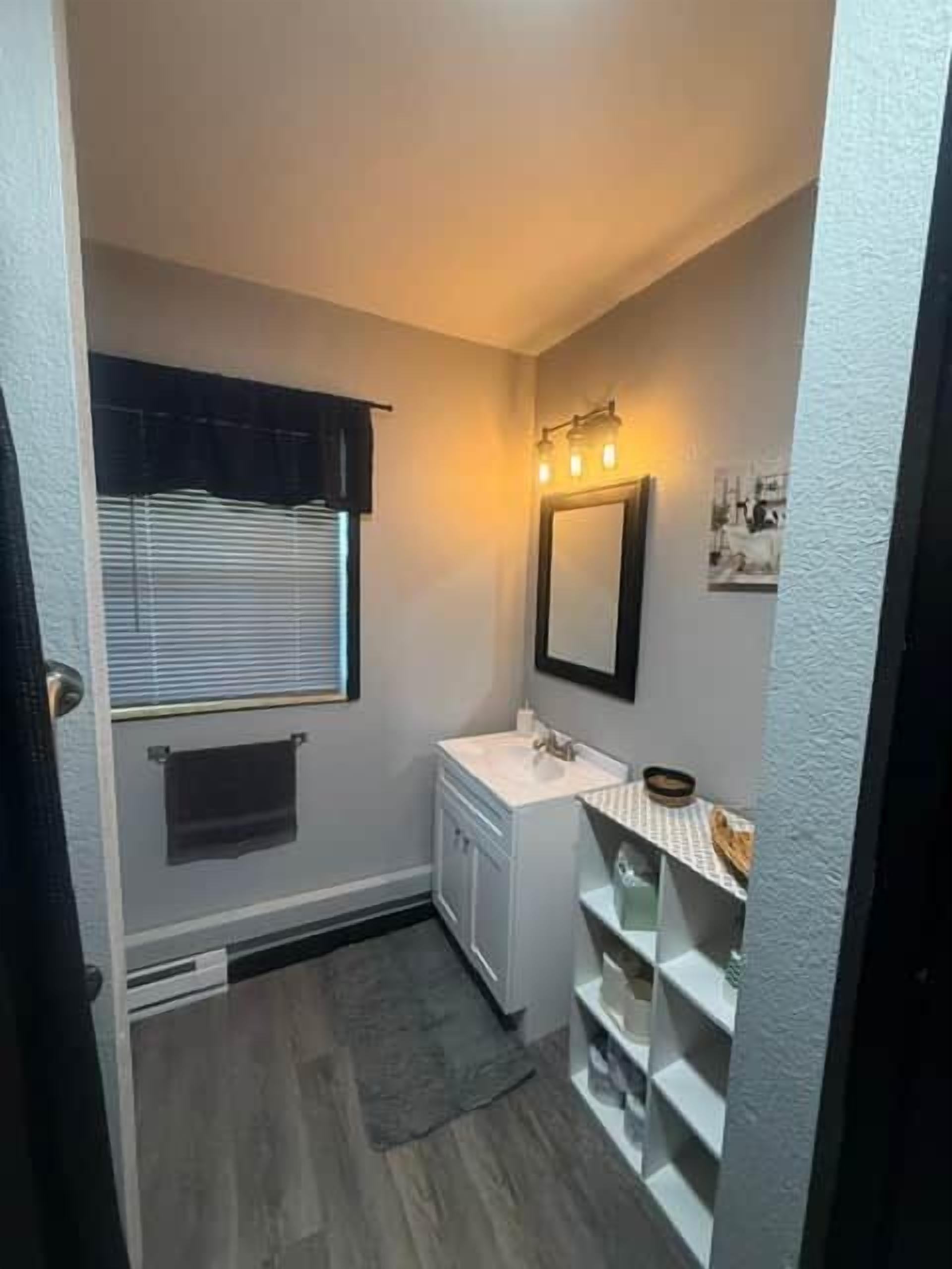 Un baño pequeño con ventana, lavamanos y espejo.