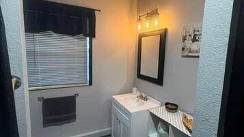 Un baño pequeño con ventana, lavamanos y espejo.