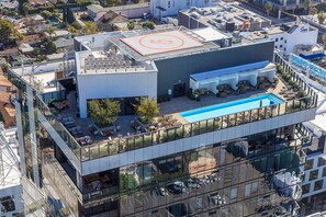 Un edificio moderno con piscina en la azotea, mobiliario exterior y fachada de vidrio.