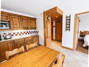 A kitchen with wooden cabinets, a tiled backsplash, and a wooden dining table with chairs. - 150m from ski slopes, 1st floor, balcony, tv, ski locker, 31m², Les Menuires (Les Menuires)