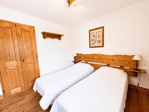 A room with two single beds, wooden wardrobe, a small shelf, and a wall-mounted picture. - 150m from ski slopes, 1st floor, balcony, tv, ski locker, 31m², Les Menuires (Les Menuires)