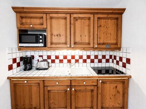 A kitchen with wooden cabinets, a microwave, a toaster, and a coffee maker. - 150m from ski slopes, 1st floor, balcony, tv, ski locker, 31m², Les Menuires (Les Menuires)