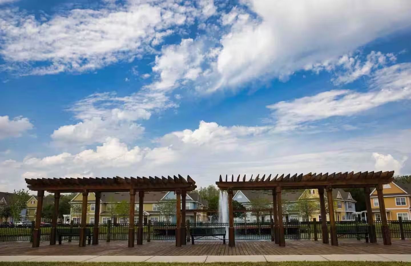 Een park met houten pergola’s, een fontein en woongebouwen op de achtergrond.