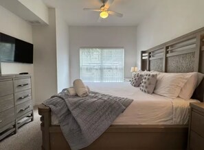 Ein Schlafzimmer mit Bett, Kommode, Deckenventilator und einem Fenster mit Jalousien.