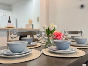 A dining table set with blue bowls, plates, and wine glasses, with a vase of flowers in the center. - Casa familiar de 3 habitaciones con piscina, cerca de Disney (Kissimmee)