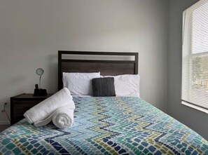 Een enkel bed met een bedovertrek met patroon, een houten hoofdbord en een nachtkastje met een lamp.