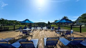 Eine Holzterrasse mit blauen Liegestühlen und Tischen, umgeben von einem schwarzen Zaun.