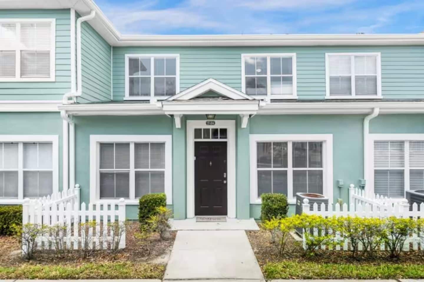 A two-story residential building with a front porch, a black door, and a white picket fence.