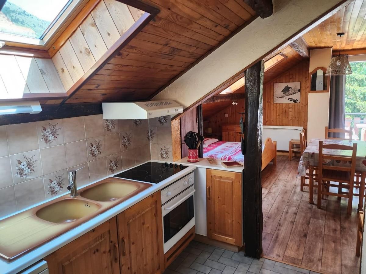 Een keuken met houten kastjes, een fornuis en een spoelbak. Er is een eethoek met een tafel en stoelen.