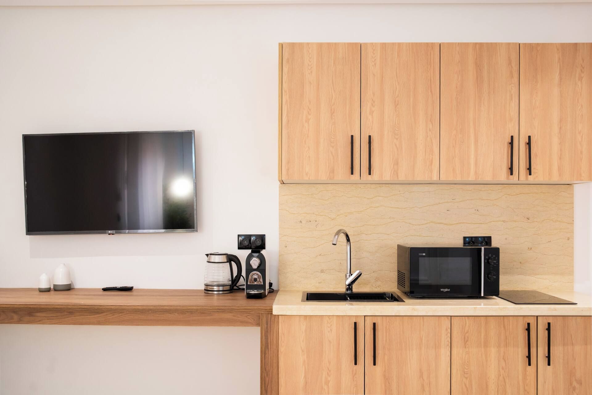 A modern kitchen with wooden cabinets, a flat-screen TV, a coffee maker, a microwave, and a sink.