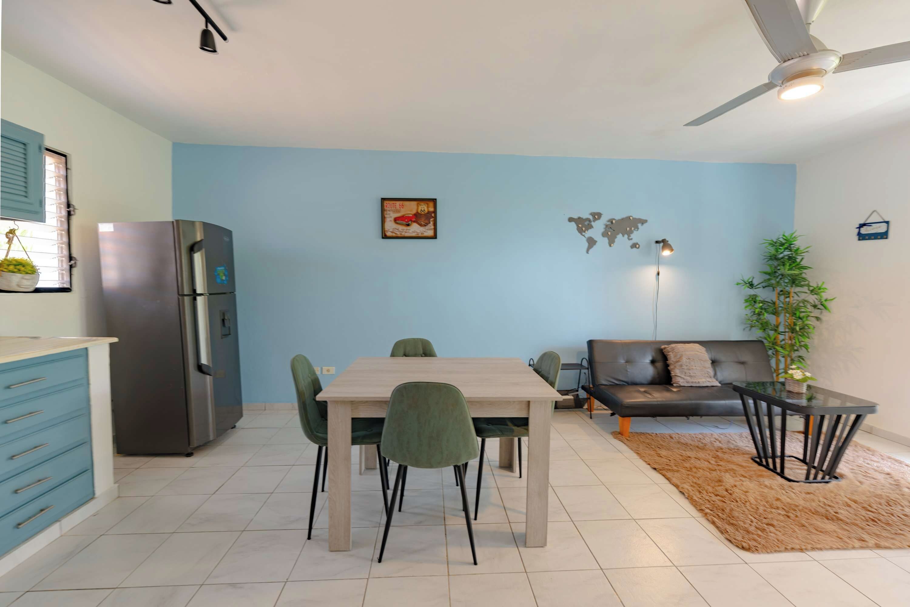 A modern kitchen with a refrigerator, a dining table with chairs, a sofa, and a world map on the wall.