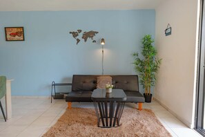 A modern living room with a sofa, a coffee table, a world map decoration, a potted plant, and a small table lamp. - Central Sosúa Studio: Beaches, Dining & More (Sosúa)