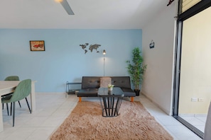 A living room with a sofa, a coffee table, a dining table with chairs, a world map on the wall, and a plant. - Central Sosúa Studio: Beaches, Dining & More (Sosúa)