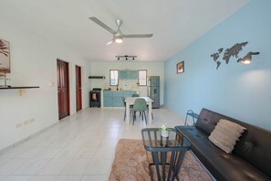 A modern living room with a sofa, a dining area with chairs, a kitchen with cabinets, and a ceiling fan. - Central Sosúa Studio: Beaches, Dining & More (Sosúa)