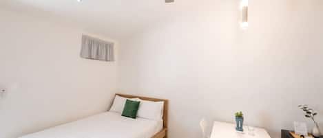 Une chambre à coucher avec un lit, un bureau, une chaise, un ventilateur de plafond et une fenêtre avec un rideau.