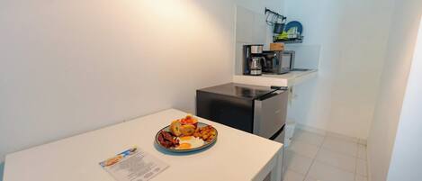 A small kitchenette with a microwave, coffee maker, and a shelf with dishes. A breakfast plate with eggs, bacon, and toast is on the counter.