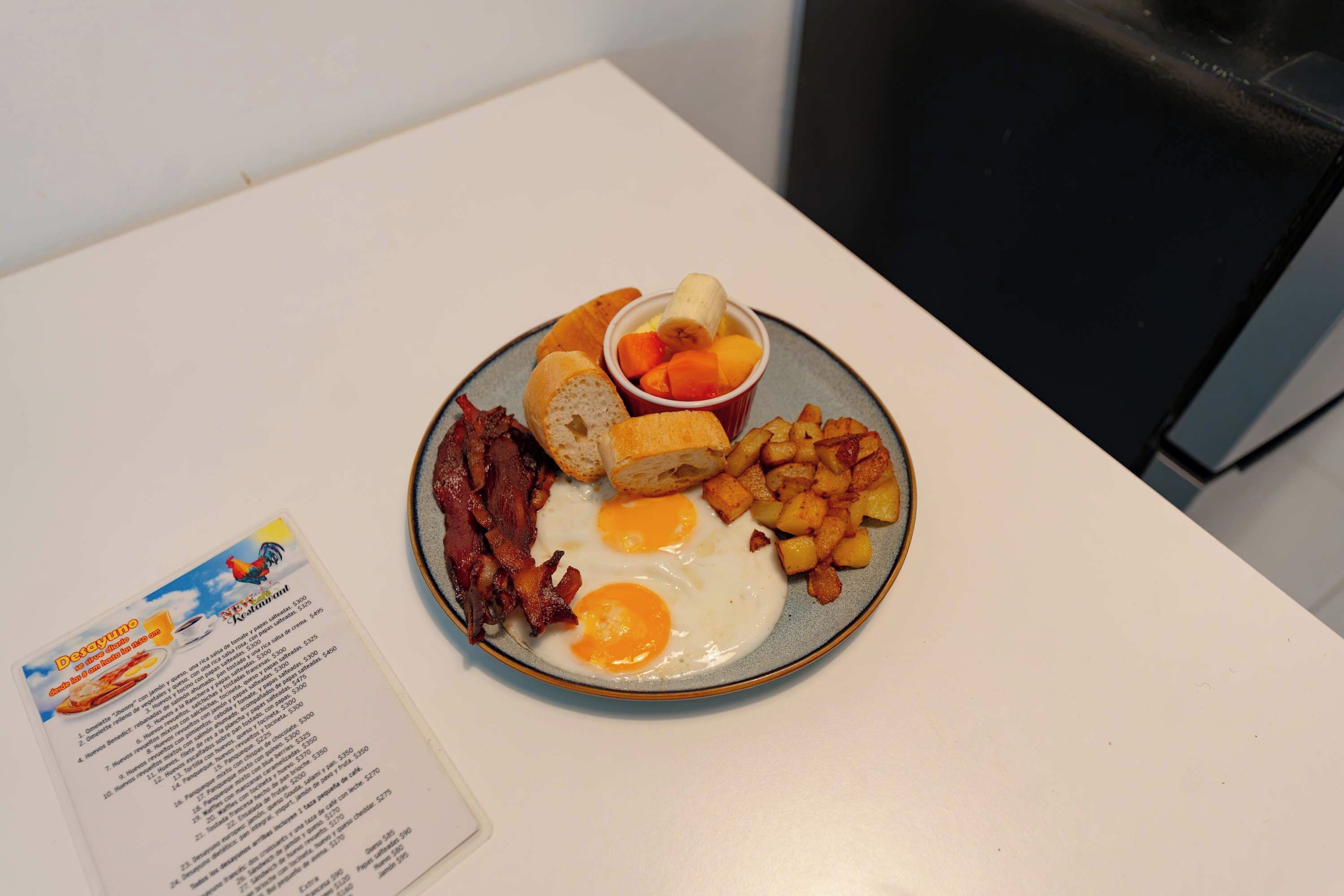 Une assiette de petit-déjeuner comprenant des œufs, du bacon, des toasts, des pommes de terre et une salade de fruits.