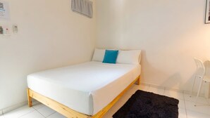 A single-bed room with a wooden frame, white bedding, a blue accent pillow, a black rug, and a white chair. - Studio in the center of Sosua (Sosúa)