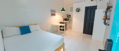 A bedroom with a bed, a desk, and a kitchenette.