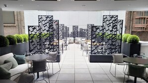 Un área de lounge moderna con sofás, mesas y sillas, separada por paneles con un estampado blanco y negro.