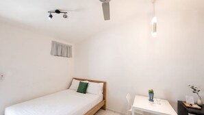 Un dormitori amb un llit, escriptori, cadira, ventilador de sostre i una finestra amb cortina.