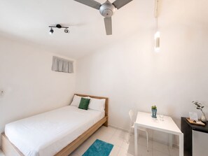 Un dormitorio con cama, escritorio, silla, ventilador de techo y ventana con cortina.