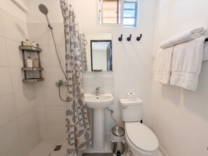 Un baño con ducha, lavamanos, inodoro y toallero.
