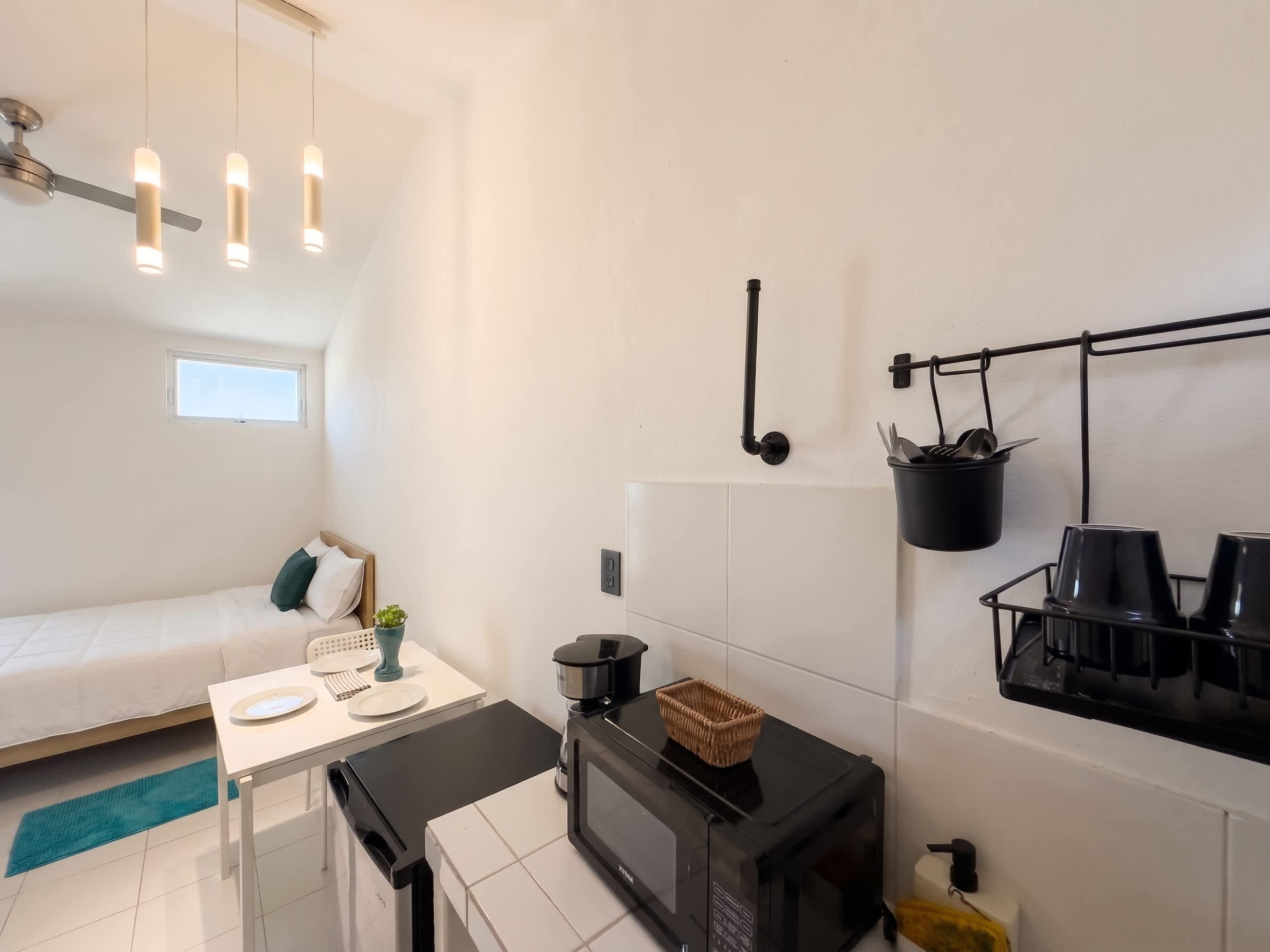 Une cuisine compacte équipée d’un four à micro-ondes, d’une petite table et d’un porte-ustensiles suspendu.