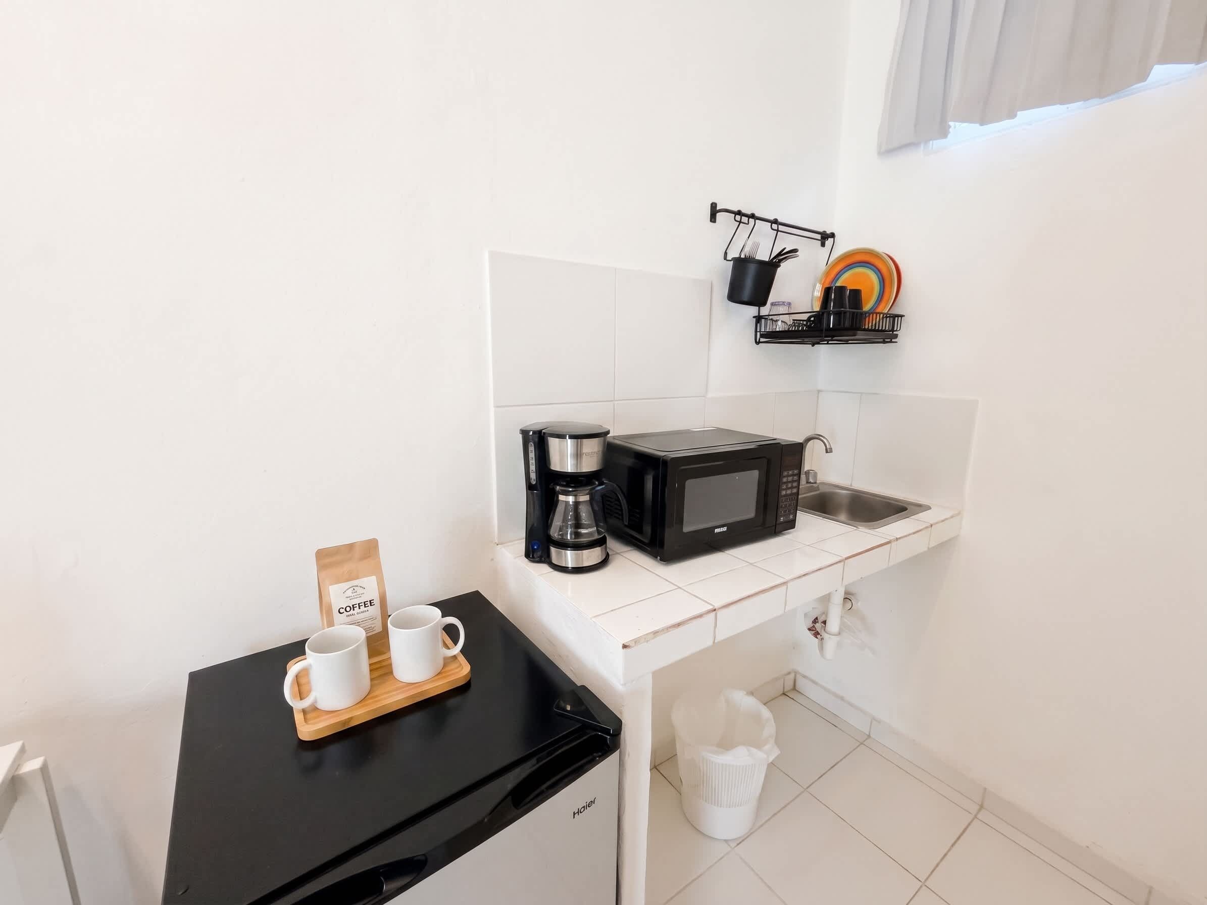 Una kitchenette compacta con cafetera, microondas y un lavamanos pequeño.