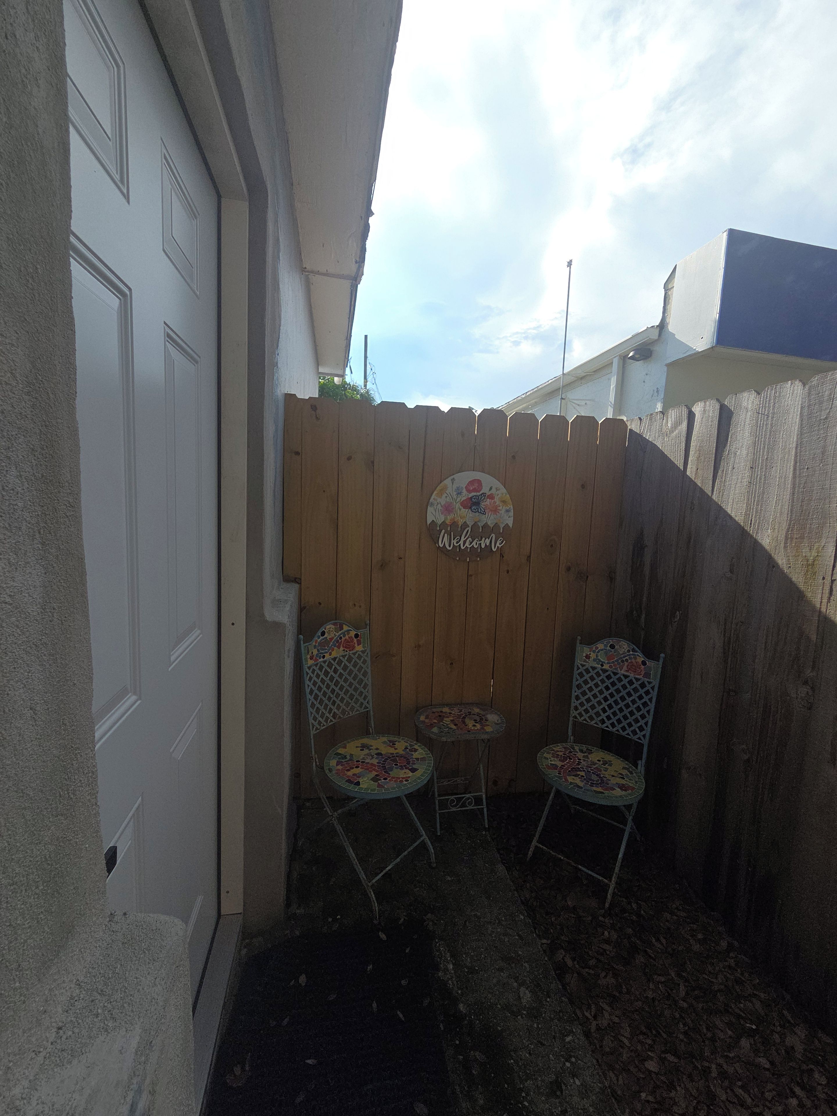A fenced outdoor area with a welcome sign, two metal chairs, and a small table.