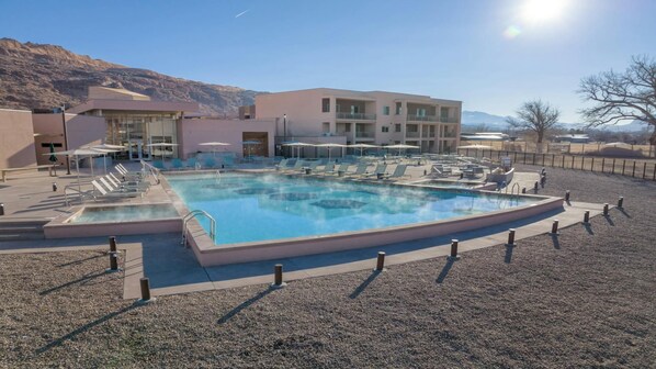 A pool area with lounge chairs and umbrellas, surrounded by buildings with a mountainous backdrop.