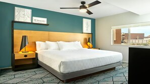 Une chambre d’hôtel avec un lit, deux tables de chevet, un ventilateur de plafond et des œuvres d’art accrochées aux murs.