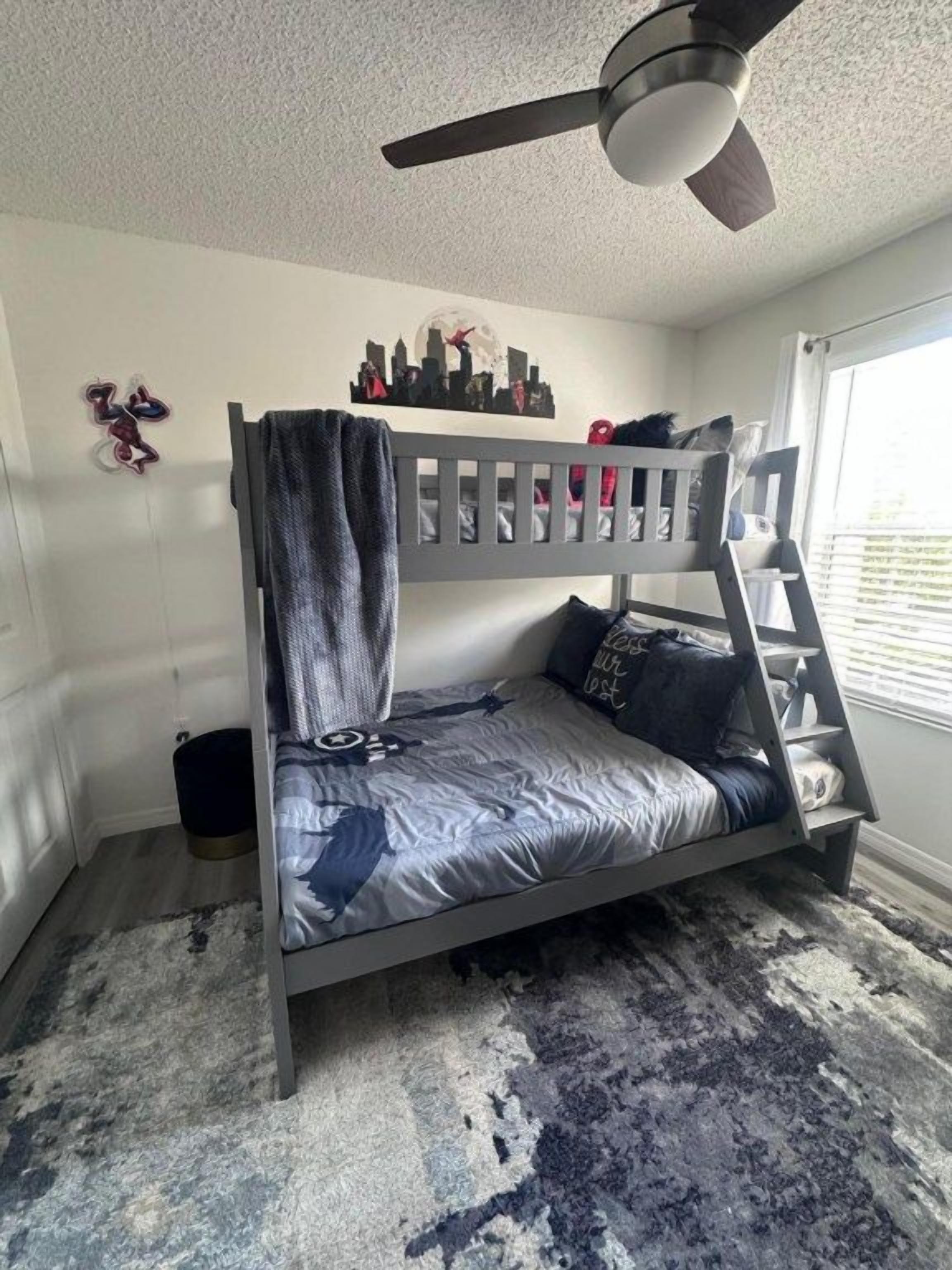 A bunk bed with a city skyline mural above it, a ceiling fan, and a window with blinds.